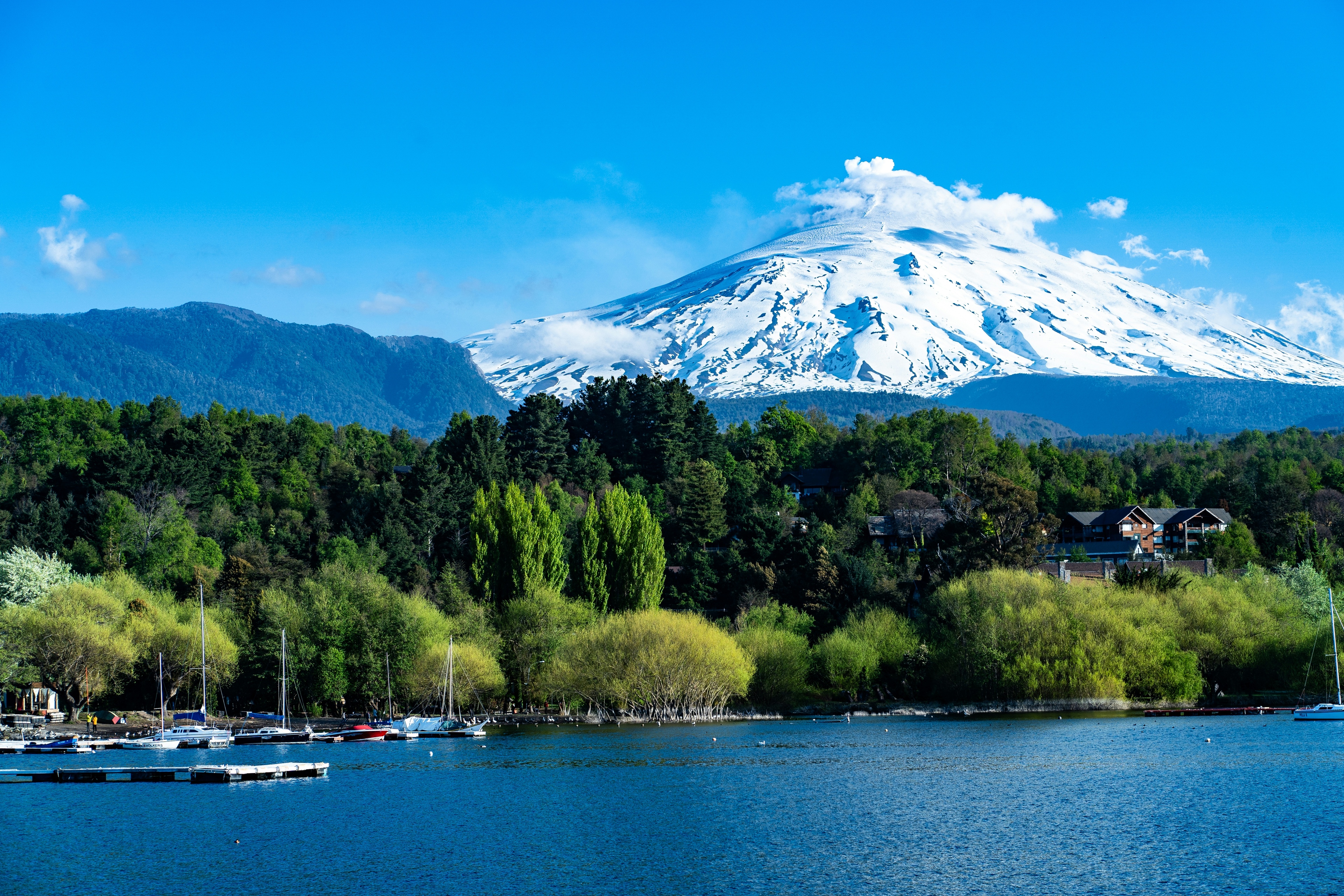 Volcán Villarrica nevado, vegetación y embarcaciones en el lago, vistos desde Pucón